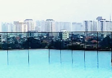A distant city skyline seen across the still surface of a rooftop pool.